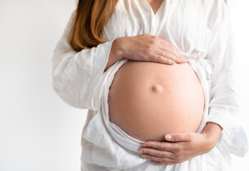 Cropped shot of unrecognizable pregnant woman touching belly standing by white wall.Copy space,...
