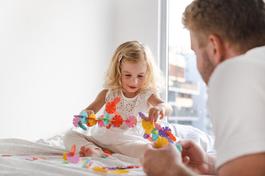 Happy Cute Caucasian Two Years Old Toddler, Girl Playing With Adult, Man With Colourful Toy Circles On Bed At Home.Father And Kid Having Fun Together. 