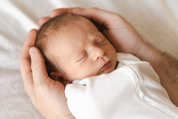 Father,young man holding caucasian hairy brunet cute newborn baby sleeping.One or two week child on bed in male hands indoors.Care, love, happiness concept. Copy space for text.