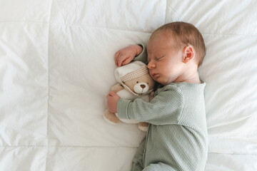Cute caucasian several days old newborn sleeping on white blanket hugging toy, teddy bear at...