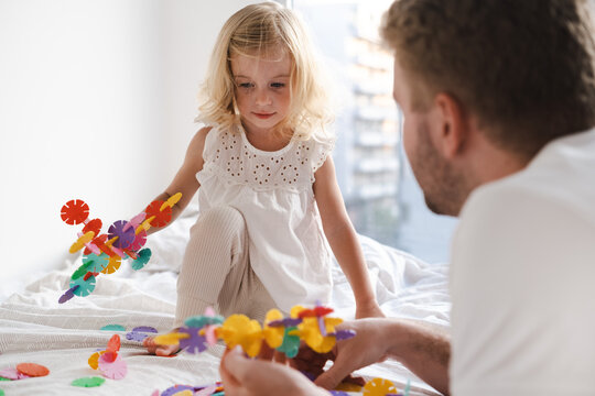 Happy Cute Caucasian Two Years Old Toddler, Girl Playing With Adult, Man With Colourful Toy Circles On Bed At Home.Father And Kid Having Fun Together. 