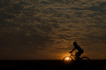 A silhouette of a cyclist who is riding in the middle of nature in the setting sun rising in the morning.