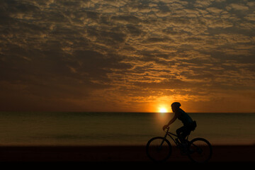 A silhouette of a cyclist riding on a beach road in the setting sun rising in the morning.