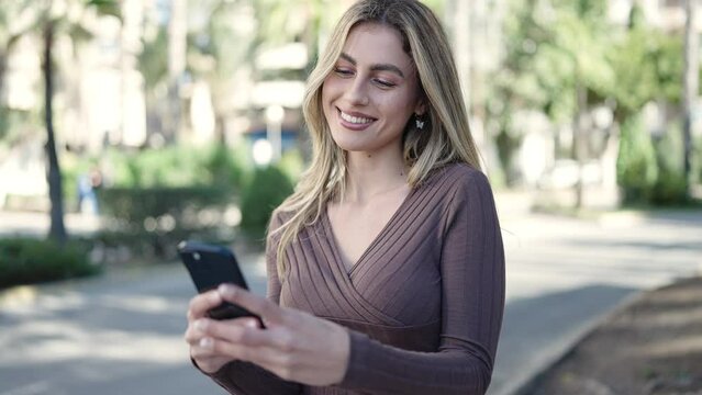 Young blonde woman smiling confident using smartphone at park