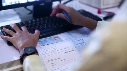 The health worker cashier is inputting patient data with an identity card at the hospital registration desk using a computer - Powered by Adobe