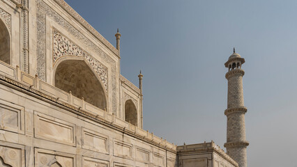 The ancient Taj Mahal. Fragment. White marble walls with arches, ornaments, inlays and precious stones. A tall minaret against the blue sky. India. Agra