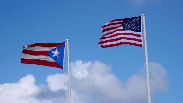 Puerto Rico and United States of America flags flapping in the wind on a sunny day with white puffy clouds.