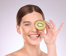 Woman, face and hand with kiwi for skincare nutrition or healthy diet against gray a studio background. Portrait of happy female smile with fruit for organic facial treatment or natural cosmetics
