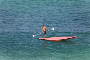 A slender strong guy standing on a SUP board looks at the surface of the water