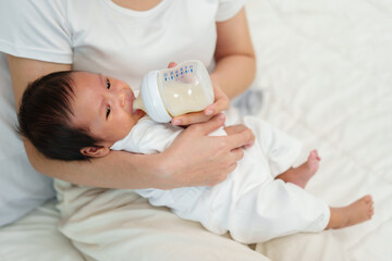 mother feeding milk bottle to her newborn baby on bed