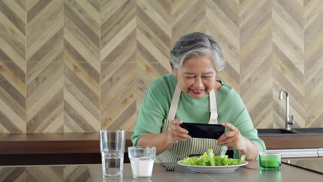 Asian healthy senior woman cooking a simple meal in the kitchen at home in the morning. Use your smartphone to take pictures of food to show off to your friends on social media. modern senior concept