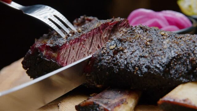The chef cuts barbecue ribs with a fork and knife to show the perfectly cooked meat - close-up