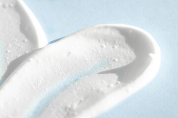 Smear of white cosmetic cream on a blue background, macro. Beauty product sample, care lotion texture.