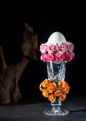 Easter egg in a glass vase with roses on black background