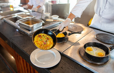 The cook is frying scrambled eggs in a frying pan in the kitchen.