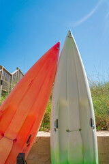 Orange and white kayaks for rent at the bay in Destin, Florida. View of orange kayak leaned towards the white kayak near the low wall and grass at the background.