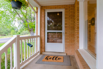 Entrance to a house with glass storm door in front of the wooden front door. An outdoor staircase leads down to the yard with grassy lawn and view of the road.