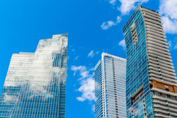 Obraz na płótnie Canvas Skyscrapers camouflaged to the sky in Miami, Florida. Three modern high-rise glass buildings with sky facade left and back on right and curved structure front to the right.