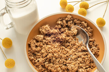 Closeup of granola bowl with a glass of milk and yellow flowers