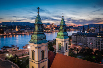 Budapest, Hungary - Aerial view of illuminated Budapest Inner-City Mother Church of Our Lady of the Assumption at dusk with Buda Castle Royal Palace at background