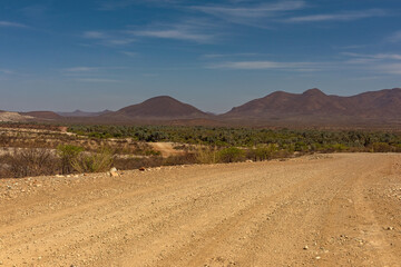 Fototapeta na wymiar The dusty gravel road along the Kunene River in northern Namibia