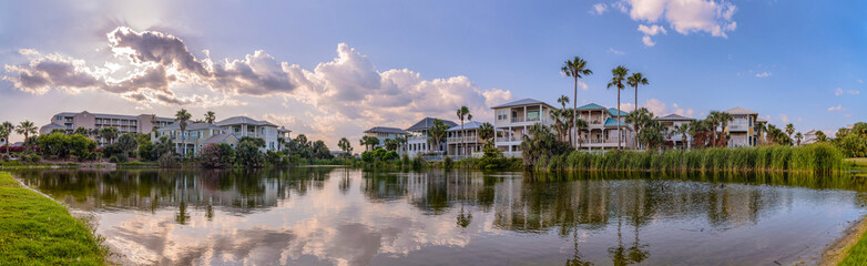 Naklejka na ściany i meble Panorama of houses and buildings around a freshwater lake in Destin Florida. Scenic nature landscape with water reflecting trees and blue sky on a sunny day.