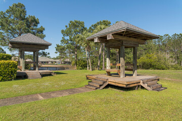 Roofed stylized picnic tables on a park with grass in a private community at Navarre, Florida. Roofed dining tables with stairs against the trees and houses at background.