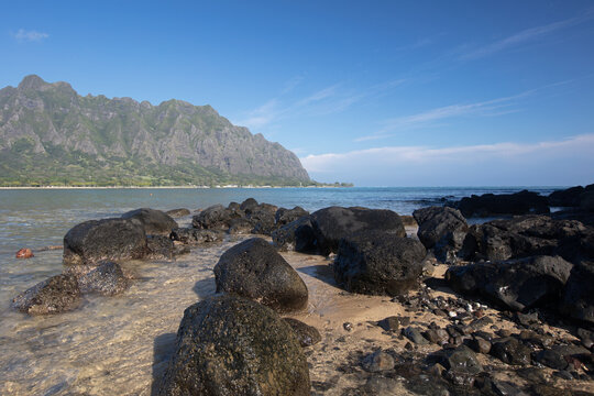 Lava rock beach on Mokolii Island [also known as Chinamans Hat] looking toward Kualoa mountains on the North Shore of Oahu Hawaii United States