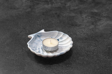 Tea candle on a shell-shaped plaster stand against a dark background.
