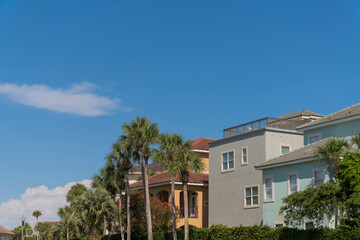 Fototapeta na wymiar Row of houses with roof tiles and palm trees outdoors in Destin, Florida. There are green and gray tiles on the right near the house with red roof near the trees on the left.