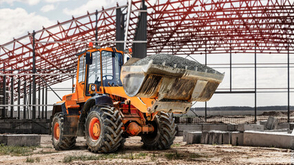 Bulldozer or loader against the backdrop of a modern frame shop under construction. Powerful wheel loader or bulldozer with a large bucket. Rental of construction equipment.