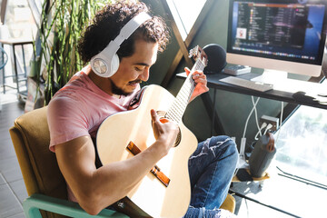 Young hispanic man musician with headphones singing and playing acoustic guitar at music studio in...