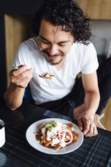 Hispanic man eating chilaquiles mexican breakfast at home apartment in Mexico Latin America