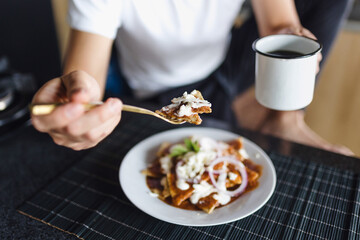 Hispanic man eating chilaquiles mexican breakfast at home apartment in Mexico Latin America