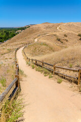 Fototapeta na wymiar Flattened dirt path with wooden barriers on the side on a mountain at Boise, Idaho. Mountain trail in the middle of grassland against the clear blue sky background.