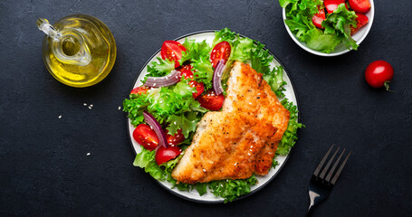 Fried cod fish with salad garnish from lettuce, cherry tomatoes and red onion with sesame seeds,...