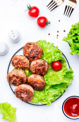 Homemade fried pork and beef meatballs with green lettuce and tomatoes, white table background, top view