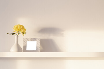 yellow chrysanthemum in vase and frame on white shelf on white background