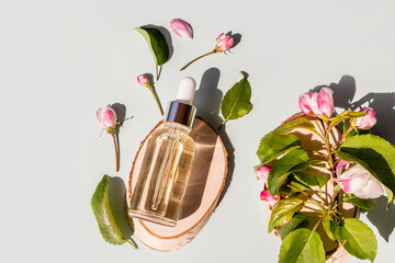 Fototapeta premium a transparent cosmetic bottle with a natural face and body care product lies on a wooden tree slice among the spring flowers of an apple tree.
