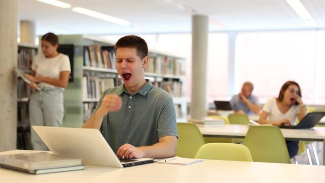 View on bored young male student with a laptop in the school library. High quality 4k footage