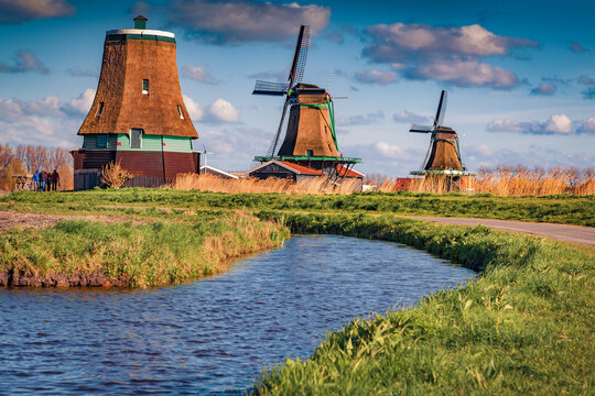 Authentic Zaandam lighthouse and windmills on the chore of famous channels in Zaanstad willage. Dramatic spring scene of Zaanse Schans, Netherlands, Europe. Traveling concept background.