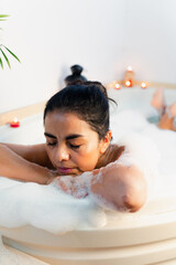 Obraz na płótnie Canvas Latin Woman relaxing deeply enjoying a splendid bath with candles in the bathtub of her home.
