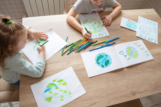 Children draw the planet Earth with pencils and felt-tip pens on album sheets for Earth Day at their home table. The concept of protecting the environment, peace on Earth.