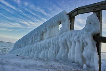 View of a frozen jetty in Travemünde in Germany with thick icicles on the railing, the cloudy sky shining in clear blue.