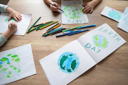 Children draw the planet Earth with pencils and felt-tip pens on album sheets for Earth Day at their home table. The concept of protecting the environment, peace on Earth.