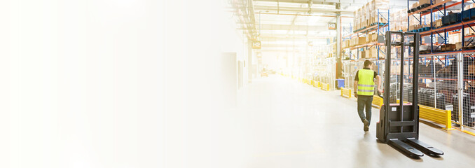 Storehouse employee in uniform working on forklift in modern automatic warehouse. Boxes are on the...