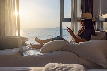 Travel insurance covers accident and medical expenses. Woman traveler with knee wrapped in medical bandage after travel accident sitting on bed in room, using smartphone and laptop to insurance online