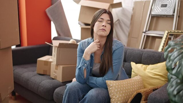 Young beautiful hispanic woman sitting on sofa with unhappy expression at new home