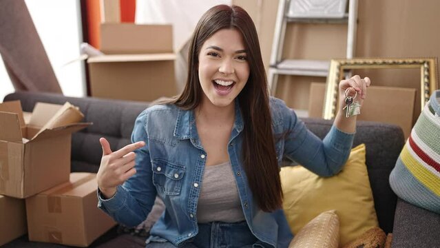Young beautiful hispanic woman smiling confident pointing with finger to key at new home