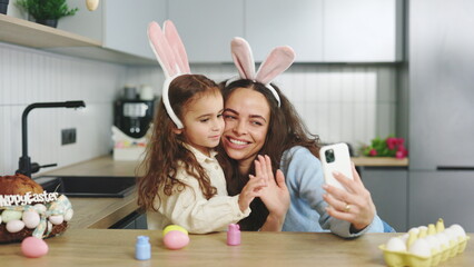 A cheerful family is preparing for the easter holiday using smartphone to video calling. Mom and...